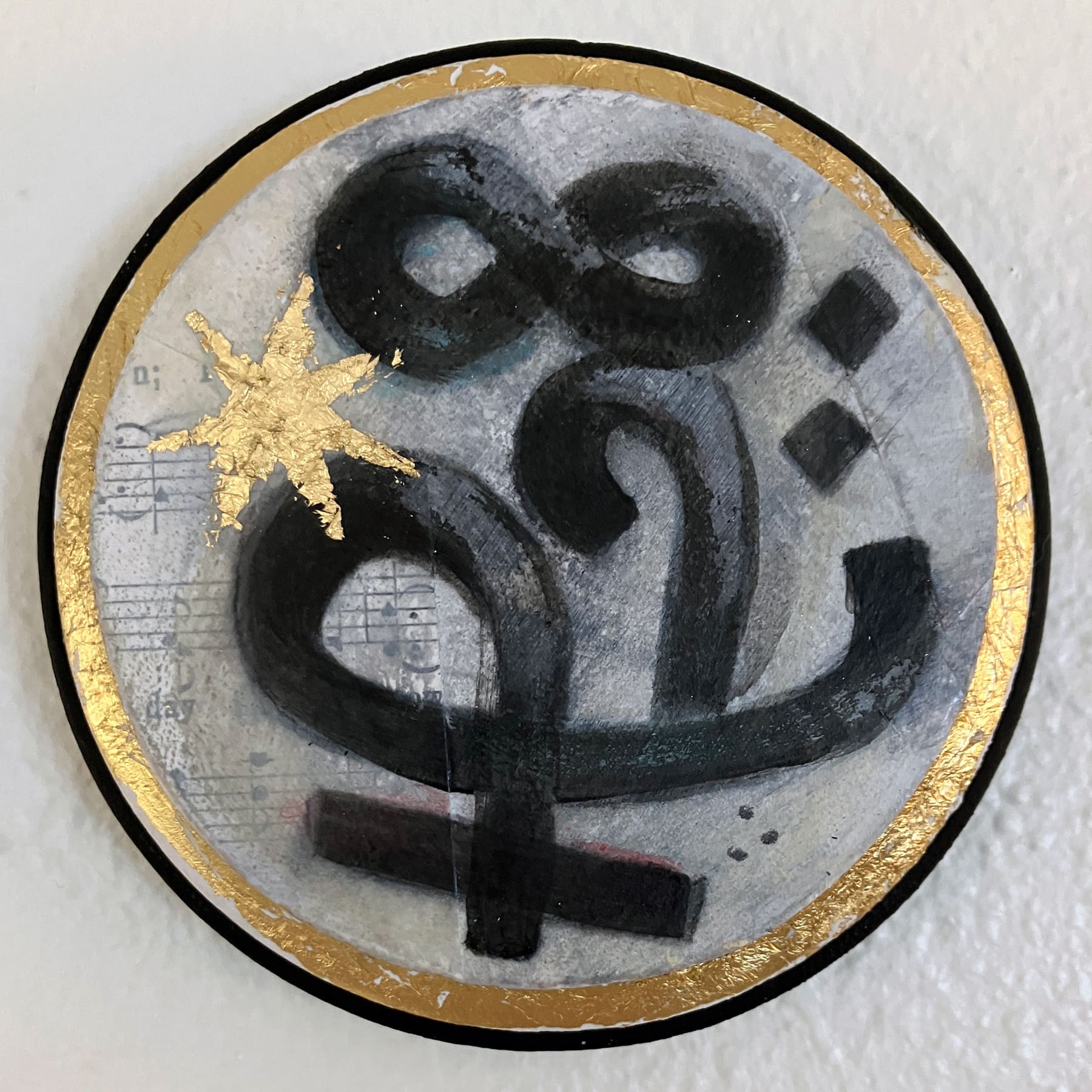 A Wormrōte sigil meaning 'learning' is highlighted with a star in gold leaf. A faint collage of hymns is scattered in the background, and the edges of the round panel are gilt in gold leaf.