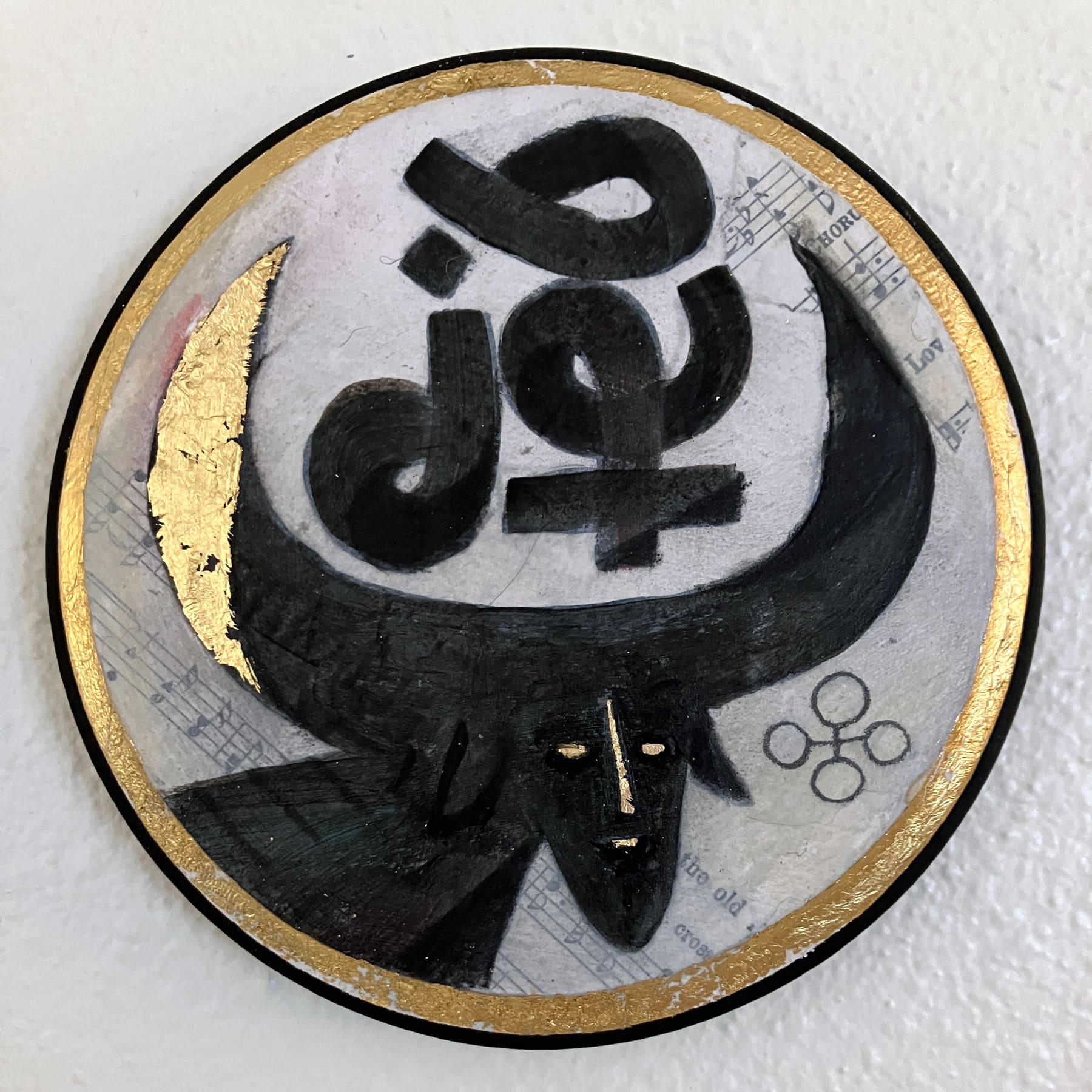 A Wormrōte sigil meaning 'blessing' sits between the horns of a black Auroch. A faint collage of hymns and pencil sigils are scattered in the background. The edges of the panel, the Auroch's face, and a horn are gilt in gold leaf.